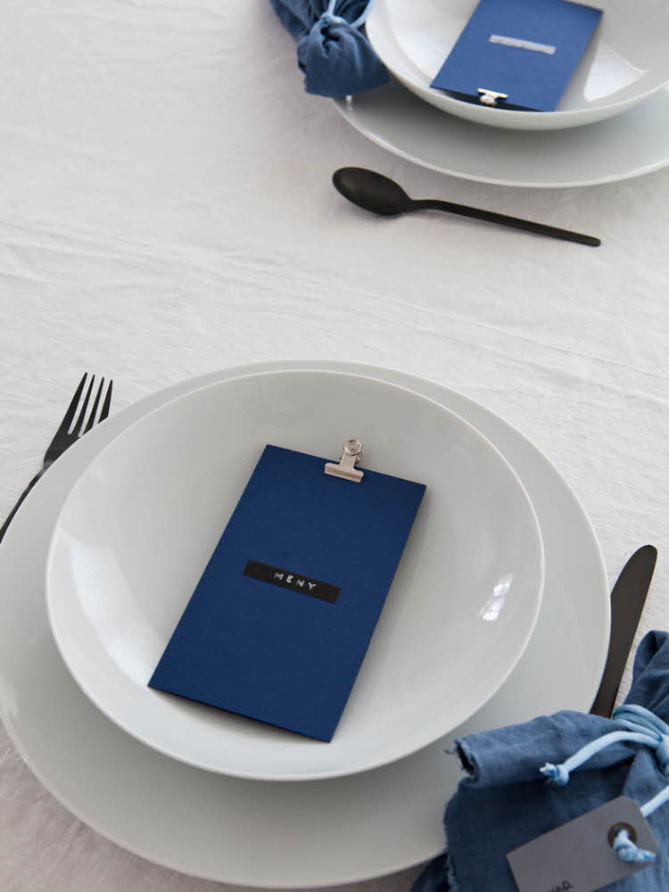 Steg 4 - bord dekket med mørkeblå tøyservietter, blått menykort og sort bestikk