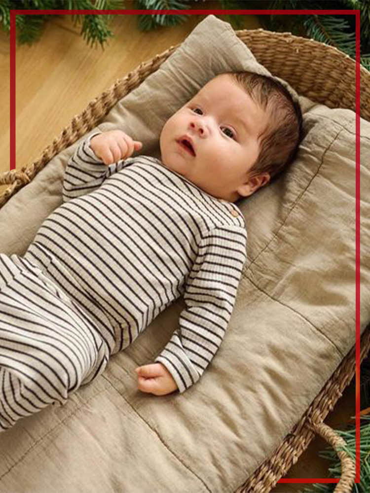 Baby ligger i en flettekurv på beige teppe og med stripete body og bukse