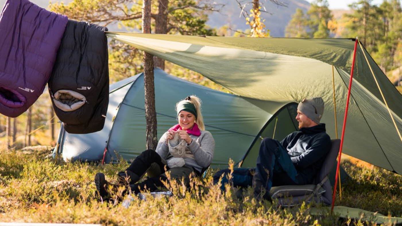 To mennesker sitter utenfor teltet sitt med en tarp over seg