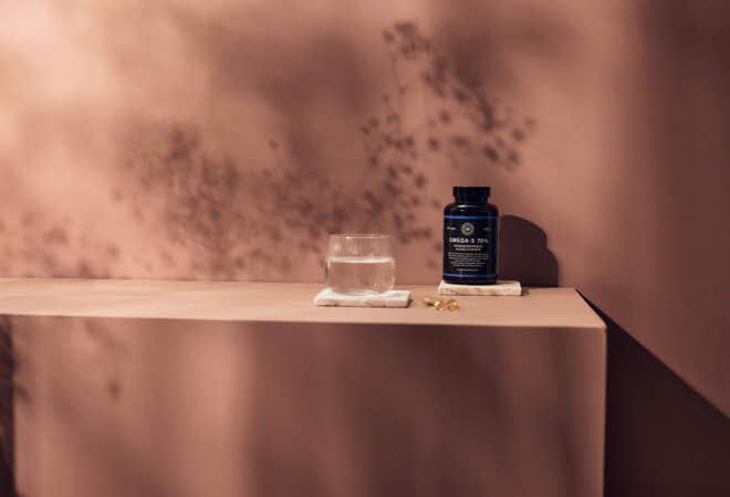 En flaske Omega-3 tilskudd, et glass vann og tre gule kapsler.