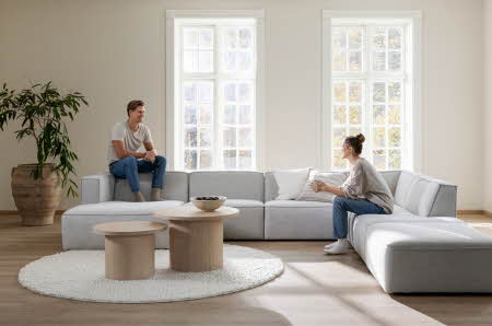 En mann og en kvinne som sitter på hver siden side av en stor grå sofa og smiler til hverandre