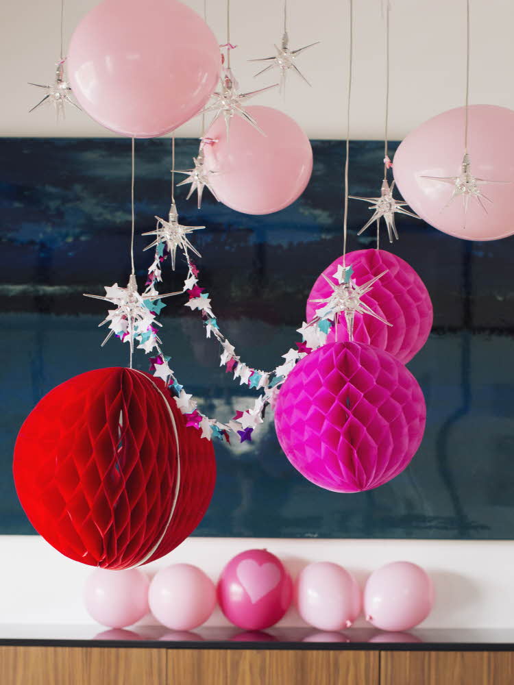 Røde og rosa ballonger, pom-poms og girlander henger i taket