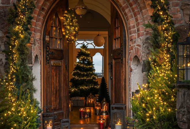 Åpen tredør pyntet med julelys og granbar.