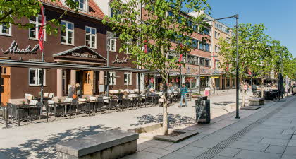 Bildet viser gågata i Lillestrøm med restauranter, butikker, grønne trer og benker.