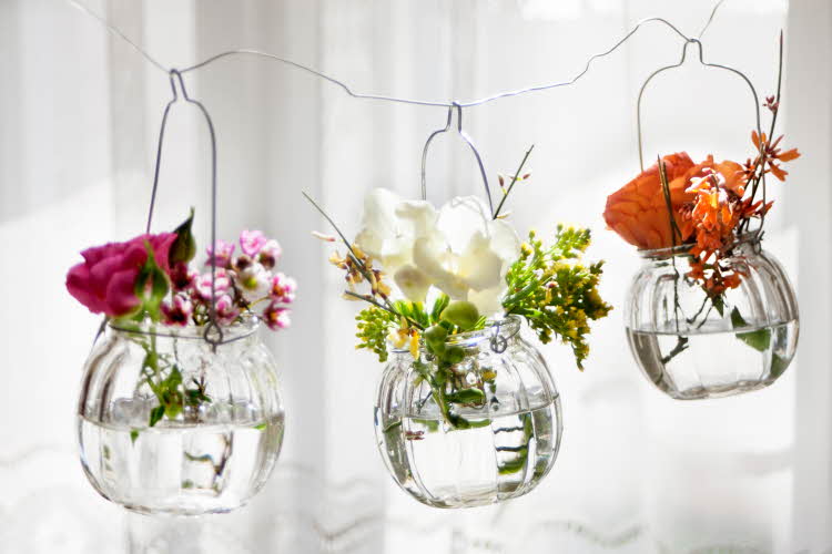Blomster plassert i små vaser som henger i en ståltråd