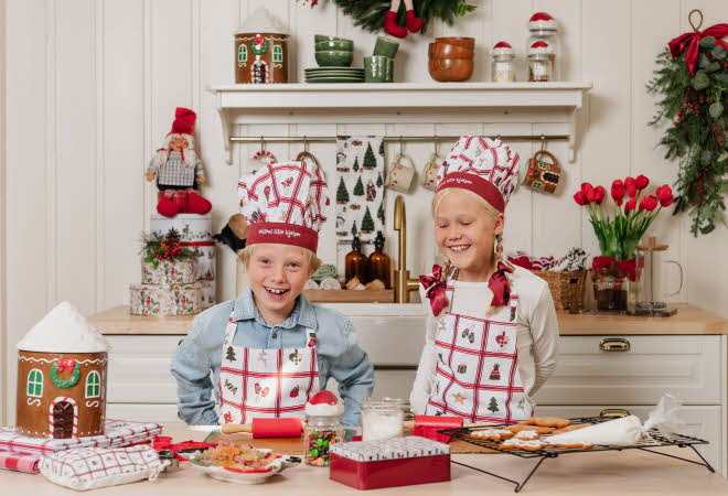 To barn står foran bakeredskaper på en kjøkken og har på seg forkle og kokkehatter