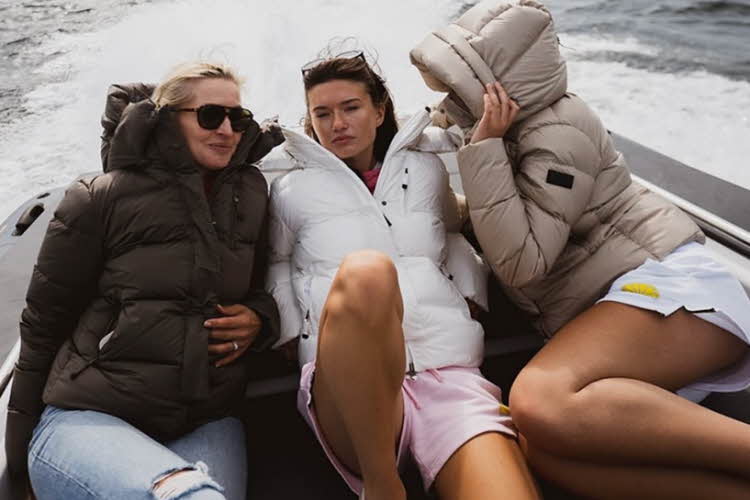 Tre kvinner i boblejakker ligger bak på en båt på vannet