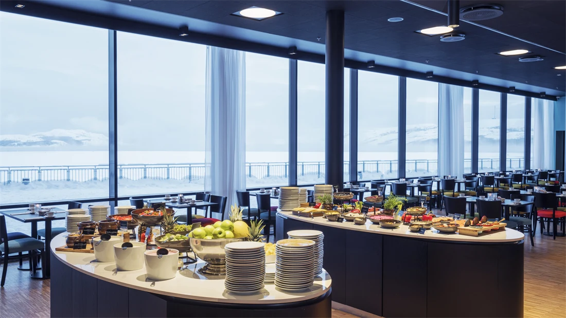 Frokostbuffet og spisebord med store vinduer som gir utsikt mot kaia og havet på Thon Hotel Kirkenes ved kaia i Kirkenes sentrum