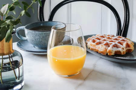 Et glass med appelsinjuice, en kopp med kaffe og en tallerken med vaffel