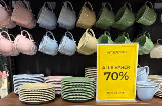 Kopper og skåler i rosa, blå og gule farger, står på en brun benk med sort bakgrunn