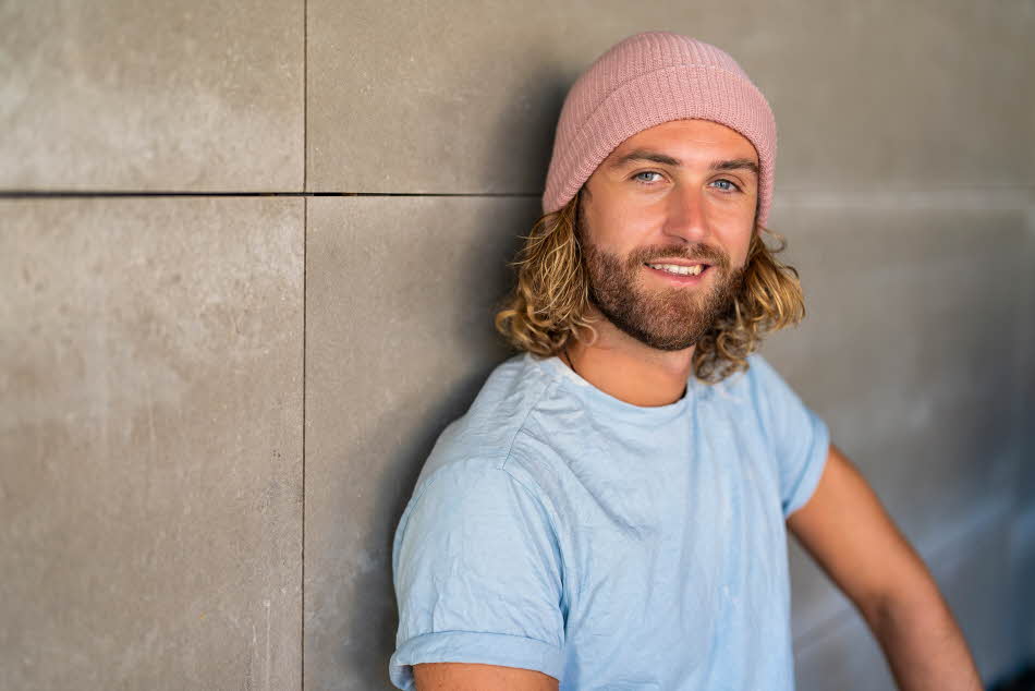 Mann med grå t-skjorte og lys rosa strikkelue smiler til kamera