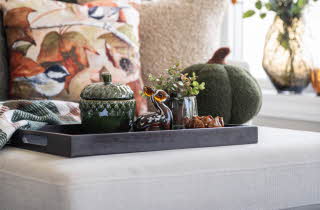Høstlig interiør med dekor på brett, inkludert keramikk, glassfigur og grønne planter.