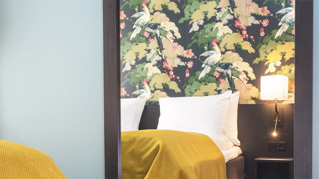 Stort vegghent speil, turkis tapet, fargerik tapet og senger med gult sengeteppe i twin rom på Thon Hotel Bristol Bergen
