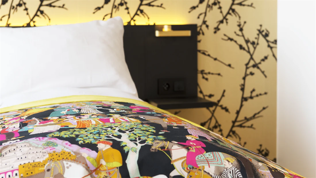 Dobbeltseng detaljbilde med mønstret gulltapet og fargerikt sengeteppe i room på Thon Hotel Rosenkrantz Oslo, som ligger i Oslo sentrum