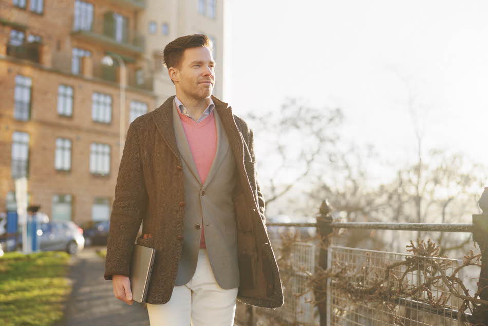 Mann med grå dressjakke, brun ytterjakke og rosa ullgenser går på gaten