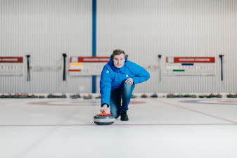 Mann som holder curling-stein på isen i en curlinghall. 