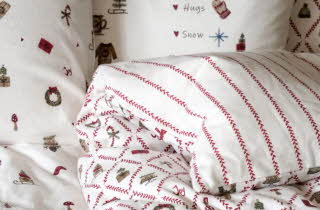 Seng med juleinspirert flanellsengetøy med røde striper og små motiv som kranser og gaver.