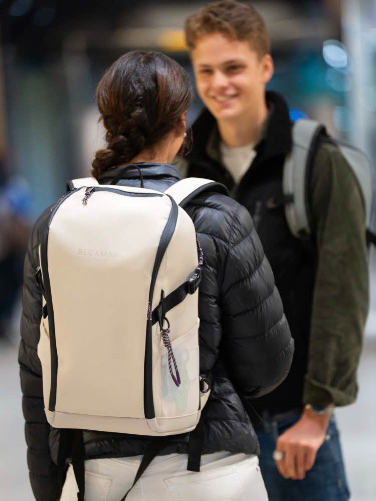 Tenåringer, jente med ryggen mot kamera med boblejakke og lyse beige skolesekk, ser på gutt med jakke og sekk.