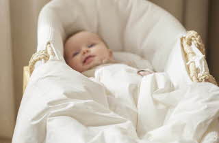 En smilende baby som ligger i en hvit babykurv.