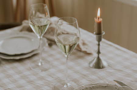 Et bord med to tallerkener, et tent stearinlys og to vinglass med hvitvin