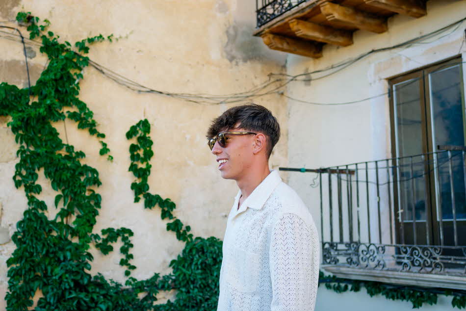 Mann med hvit heklet skjorte og solbriller sett fra siden utendørs