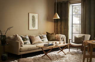 En stue med en beige sofa, en lenestol og et stuebord