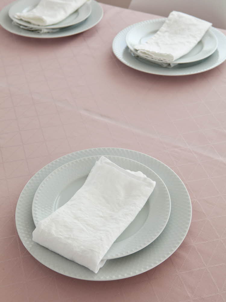 Steg en - Bord dekket med tallerkener på en rosa duk  Steg 2 - Bord dekket med tallerkener og hvit linservietter på en rosa duk 