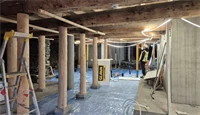 Takbjelker, nye og gamle trepæler, betongpæler og -vegg, presenning på gulv. Del av totalrenovering av Kjøpmannsgata 15 i Trondheim.