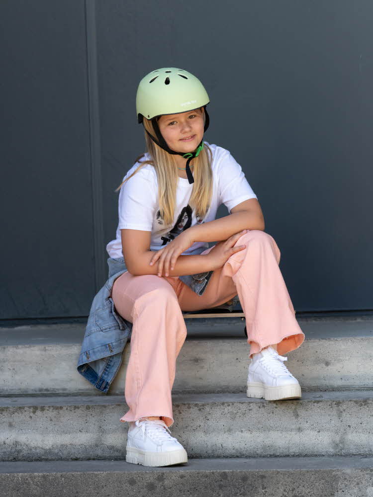 Jente som sitter i trapp på et skateboard og har på hjelm Gutt som kjører sparkesykkel og har på hjelm