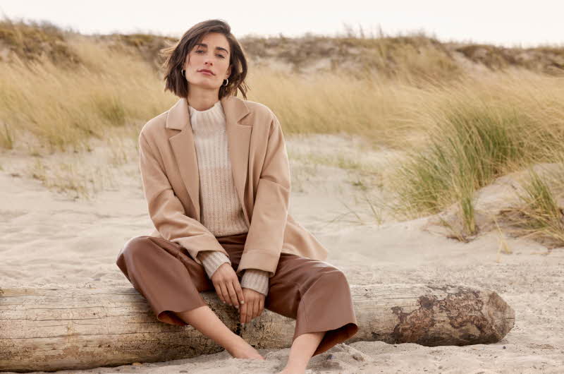 dame i beige kåpe sitter på en strand