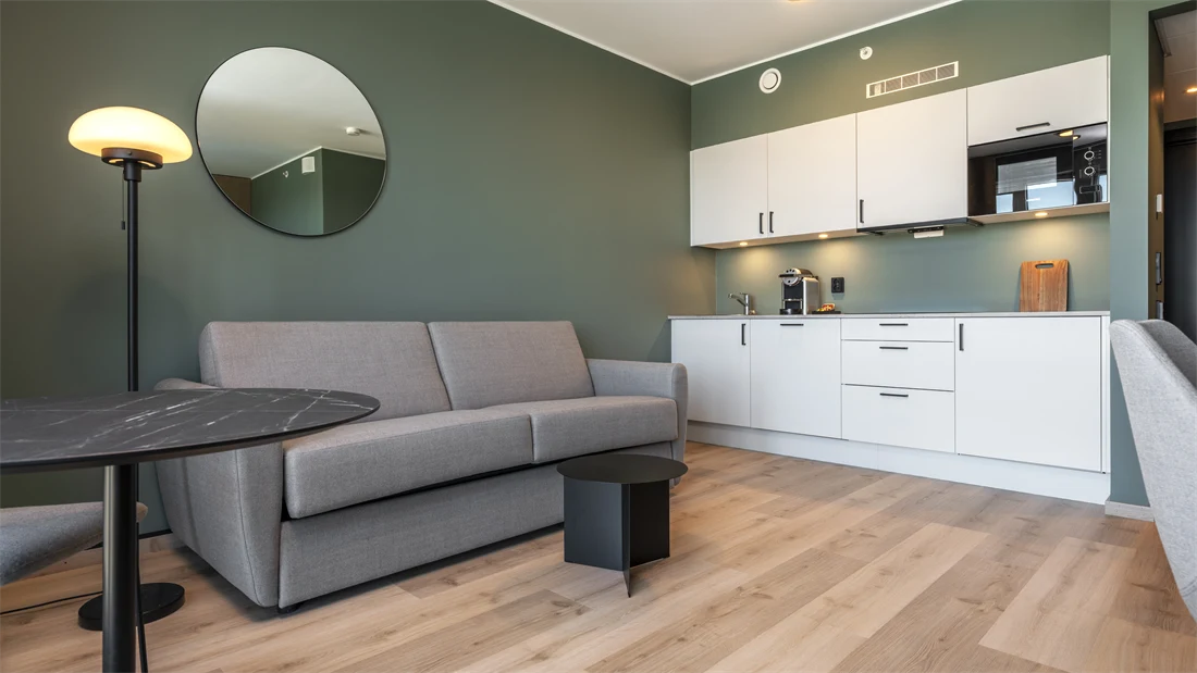Superior rom med kjøkken krok, sofa, grønne vegger, parkett, og rundt speil på veggen 