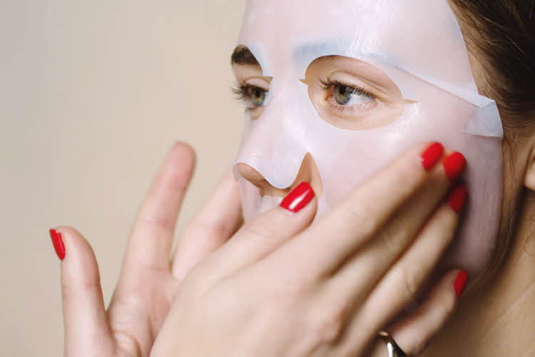 Ansiktsmaske påføres med hender med røde negler 