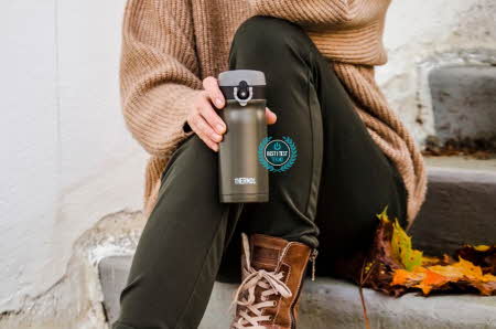 En person som sitter på en trapp ute med en termoskopp i hånden.