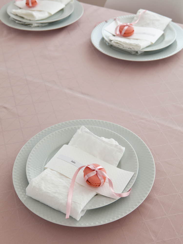 Steg fire - Bord dekket med tallerkener og hvit linservietter og en rosa makron på en rosa duk 