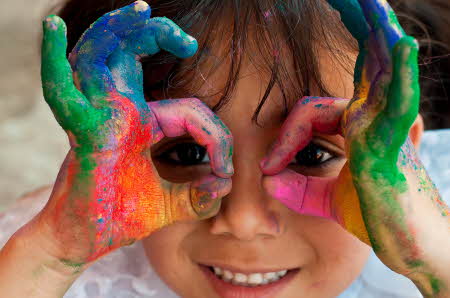 En jente med hendene dekket av flerfarget maling