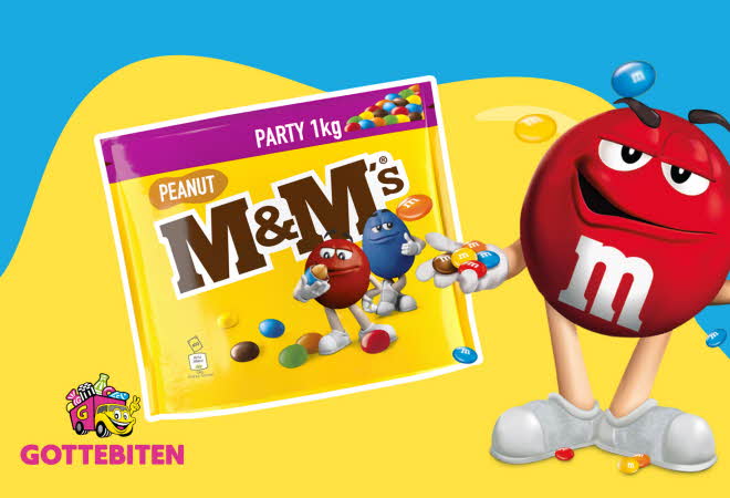 En pose med M&M's og en stor M&M med armer, bein og ansikt som står ved siden av