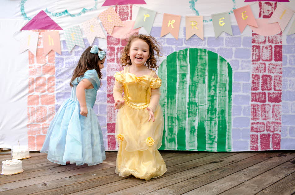 To jenter kledd ut som prinsesser hopper foran et lateslott