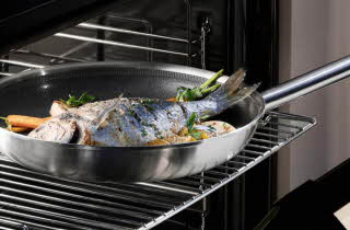 En stekepanne med en hel fisk i som står i stekeovnen.