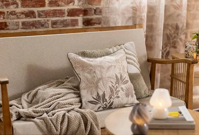En sofa med to pynteputer og et pledd
