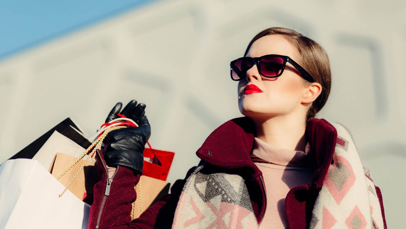 Dame med shoppingposer og solbriller ser mot himmelen