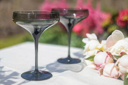 To Noir cocktailglass fra Magnor som står på et bord ute ved siden av en bukett