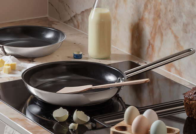 Kjøkken med to stekepanner, egg og melk på benken.