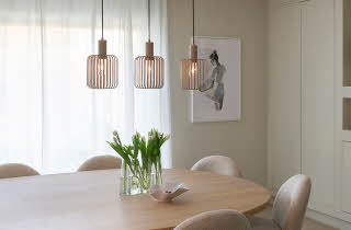 En spisestue med tre lamper som henger over et spisestuebord med en vase med blomster på
