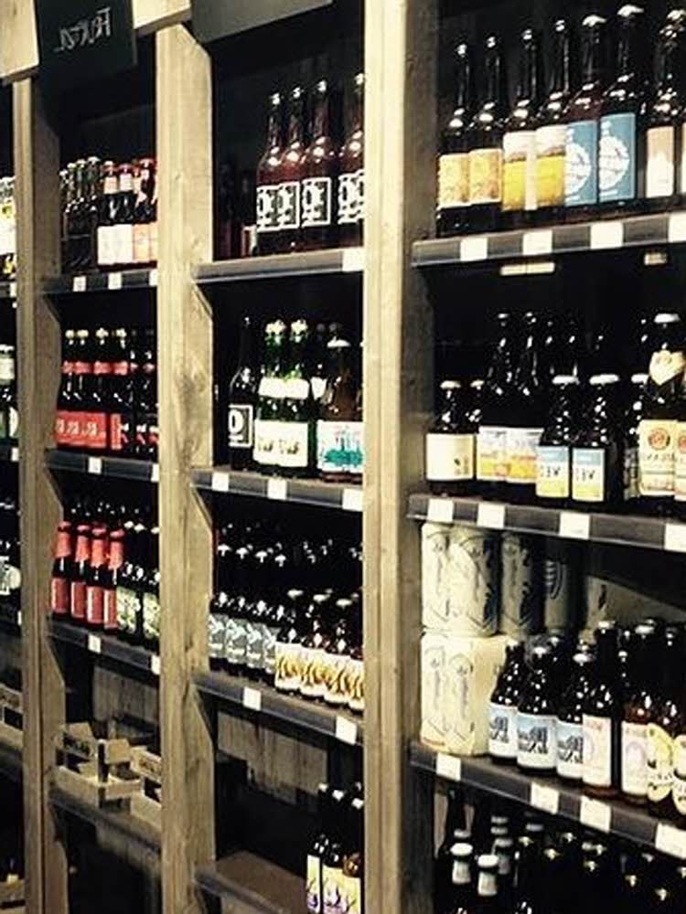 store hylle fulle av ølflasker butikkleder står foran ølhyller Gulating logo