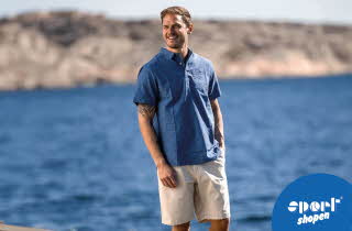 En mann i blå t-skjorte og beige shorts som står foran vannet