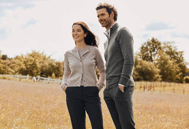 En mann i grå genser og en kvinne i beige cardigan står ute på en åker