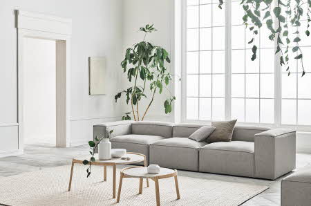 Lys stue med grønne planter, grå sofa og to stuebord