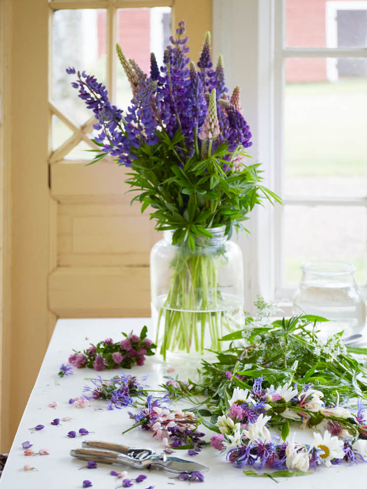 Blomsterbukett i lilla og grønt arrangeres på bord