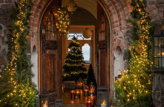 Åpen tredør pyntet med julelys og granbar.