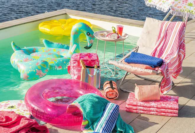 Badering, håndklær, strandbag og strandstol som står ved siden av et basseng som har to oppblåsbare flåter